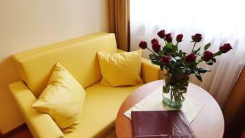A yellow sofa with matching cushions, a vase with red roses, and a closed purple notebook on a round table.