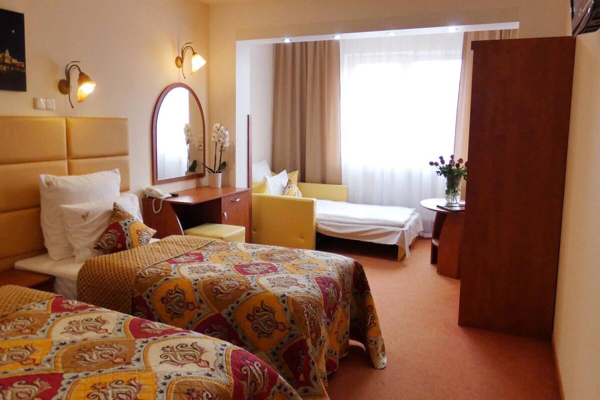 Ein Hotelzimmer mit zwei Betten, einem Schreibtisch, einem Stuhl, einem Spiegel und einem Fenster mit Vorhängen.