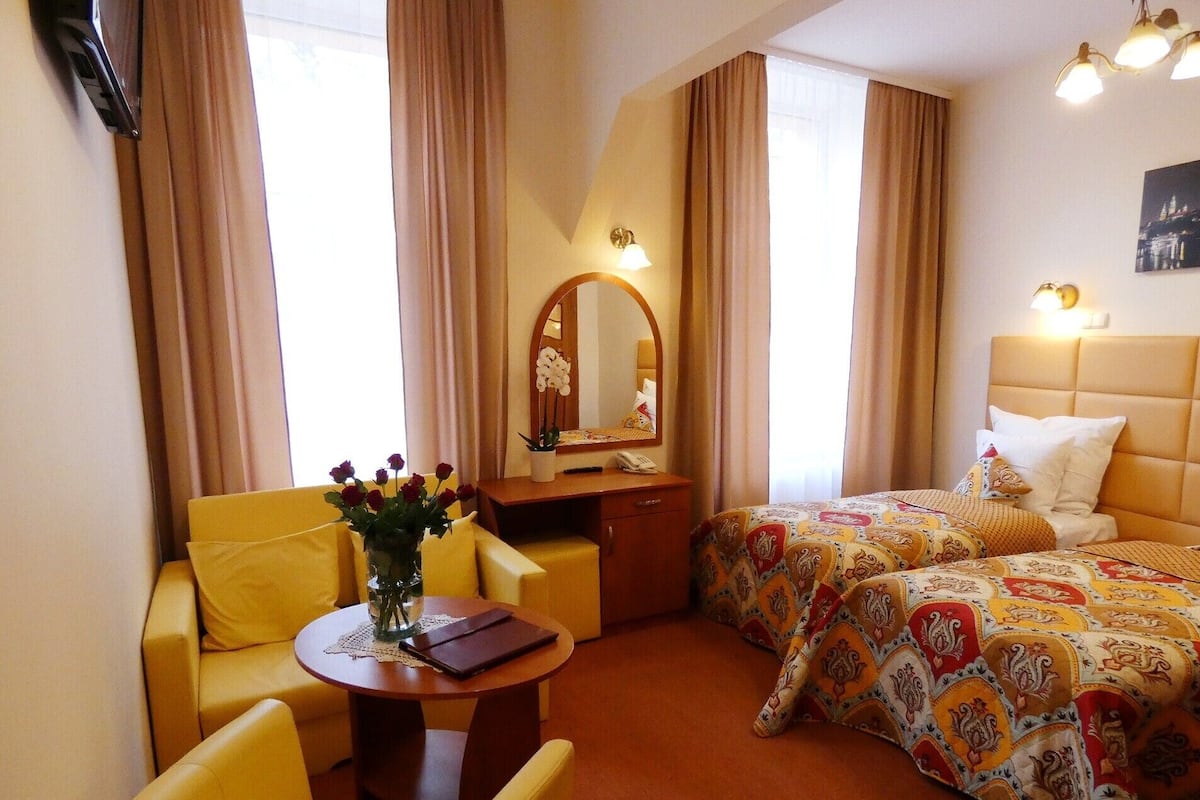 Ein Hotelzimmer mit Bett, Schreibtisch mit Stuhl, einem kleinen Tisch mit Blumenvase und einem Spiegel.