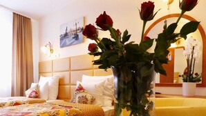 A hotel room with a bed, a vase of red roses, a painting on the wall, and a mirror reflecting the room. - Aparthotel Adler (Kraków)