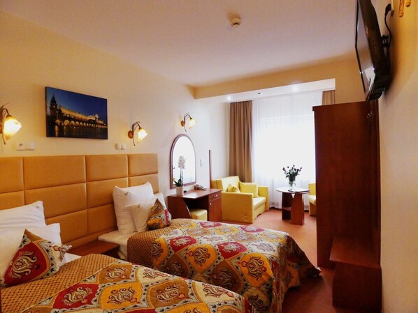 A hotel room with two beds, a sitting area with a sofa and armchairs, a desk, a mirror, and a television.