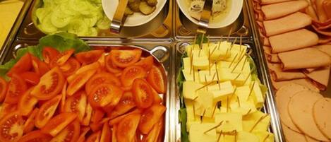 Un bufé con diferentes opciones de comida, incluyendo tomates en rodajas, cubos de queso y otros platos.