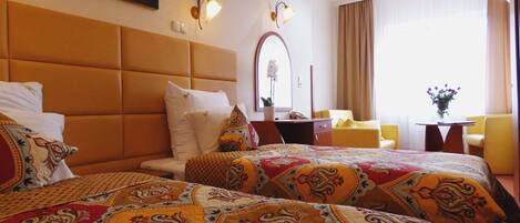 A hotel room with a large bed, a desk, a chair, and a window with curtains.