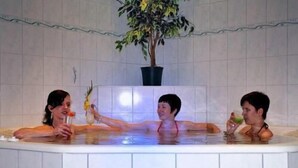 Un jacuzzi con tres personas, una planta en maceta y paredes de azulejos.