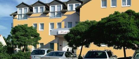 Un edificio de hotel con fachada amarilla, varias ventanas y un letrero que dice “HOTEL”. Hay coches estacionados en la parte delantera.