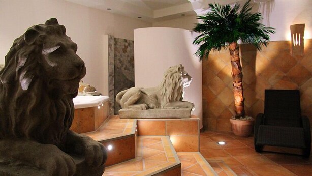 Vestíbulo con una estatua de león, una palmera y una silla moderna.