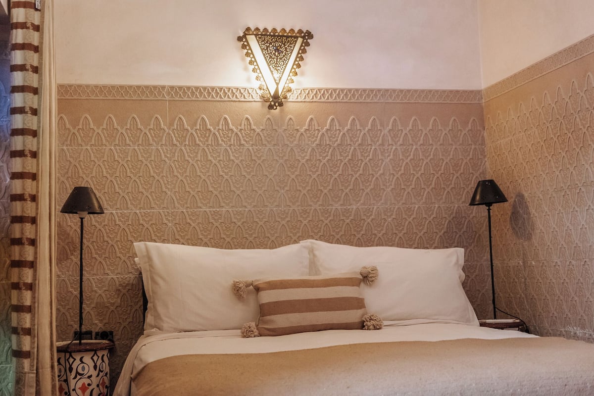 Un lit bien fait, agrémenté d’oreillers à rayures, un motif décoratif sur le mur et un luminaire fixé au mur.