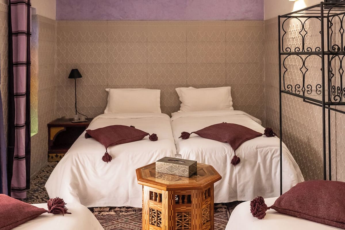Une chambre d’hôtel avec deux lits, une petite table d’appoint en bois, un luminaire suspendu et une moquette à motifs.