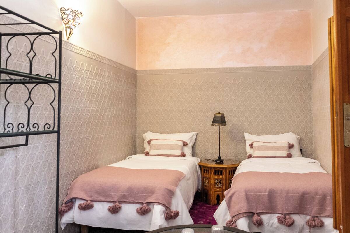 Une petite chambre accueillante, avec deux lits, une table de chevet, une lampe et un mur décoratif.