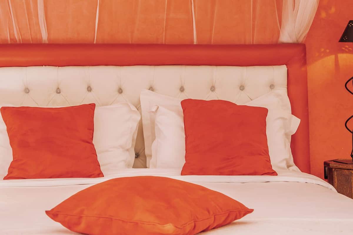 Un lit avec une literie blanche et orange, une tête de lit blanche et des rideaux orange.