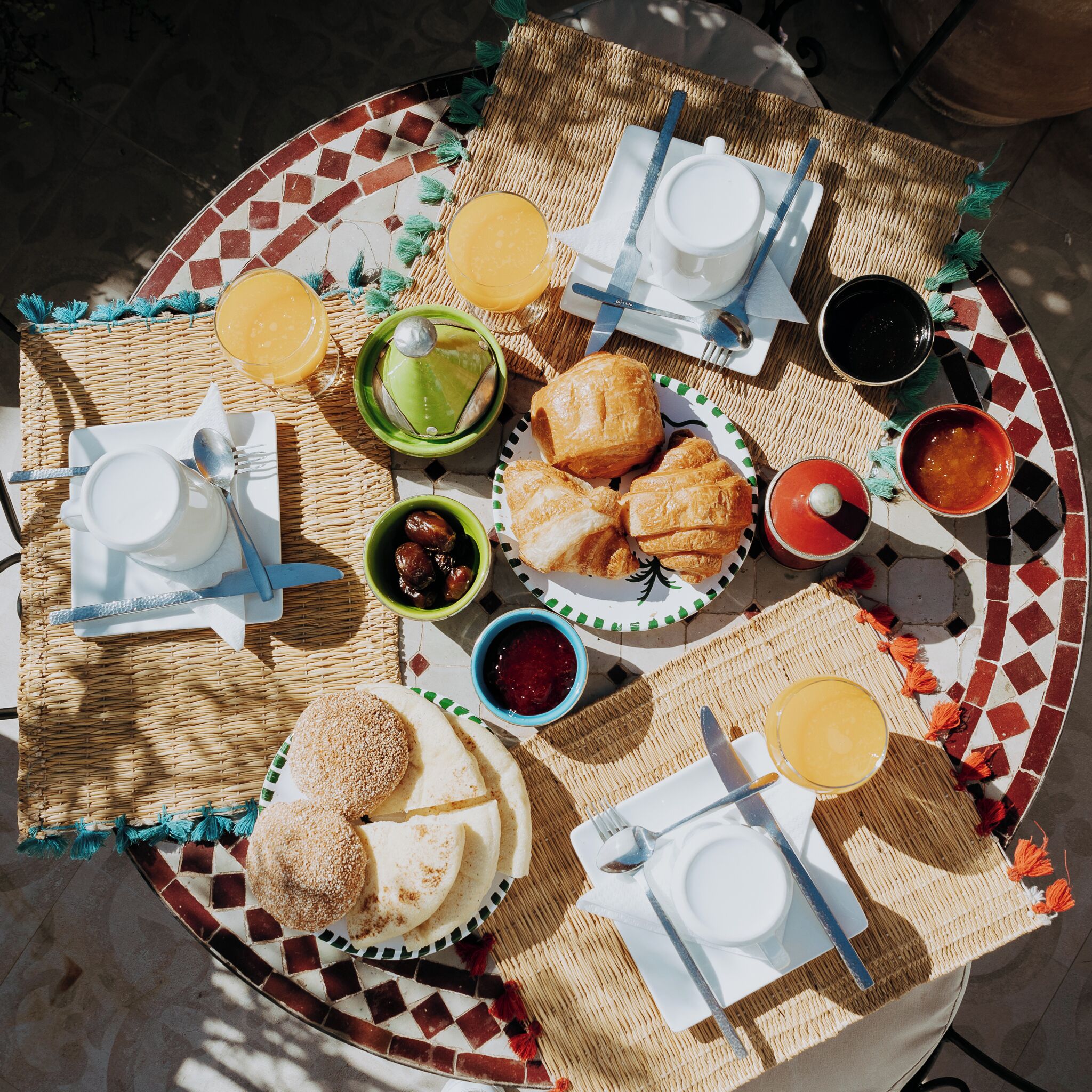 A round dining table with a mosaic pattern, various breakfast items, and a woven placemat.