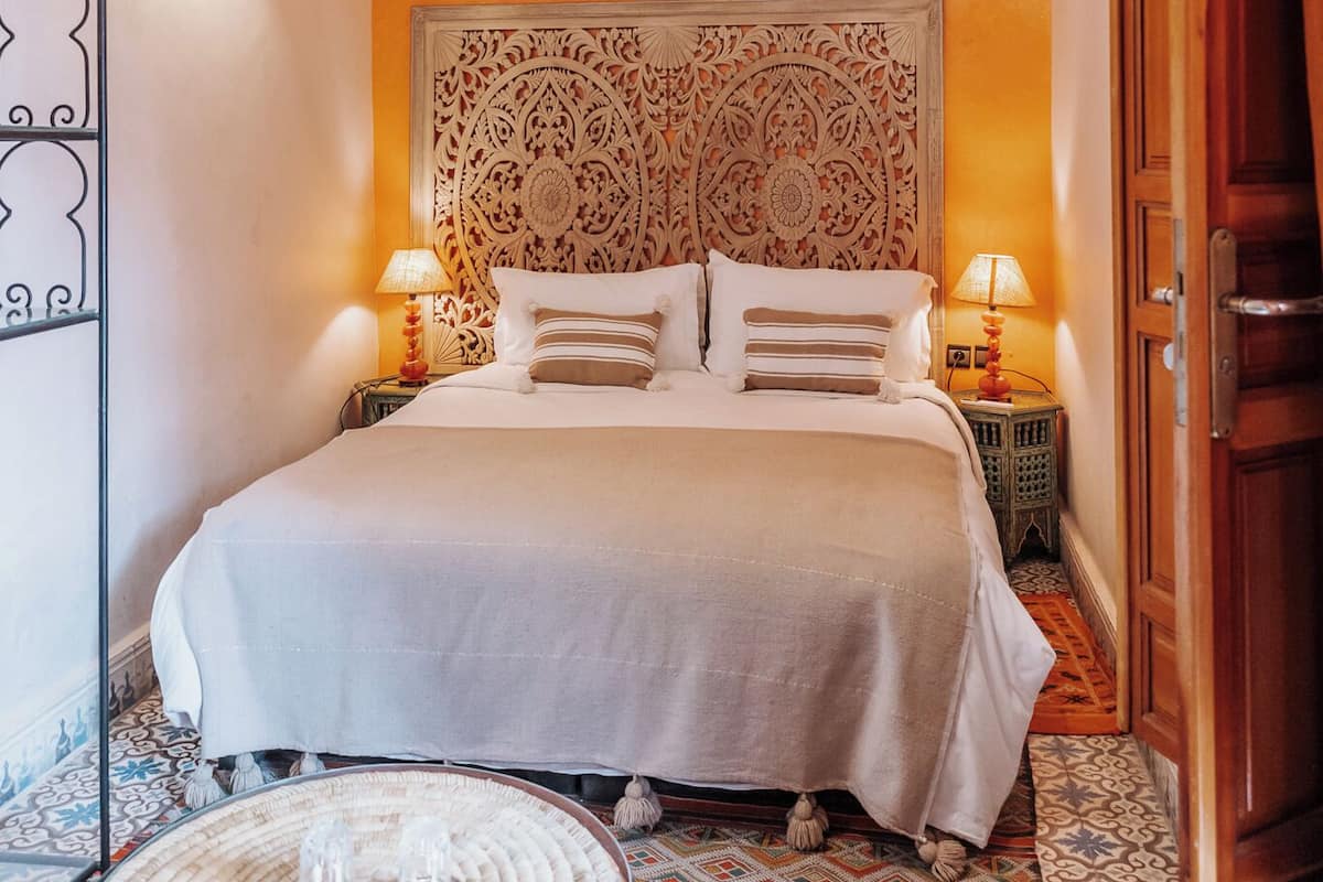 Une chambre à coucher bien aménagée, avec une tête de lit à motifs, deux lampes de chevet et une lampe de sol décorative.