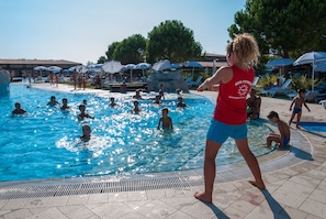 Une piscine où l’on voit des gens dans l’eau et sur le bord, entourée de parasols et de chaises longues.