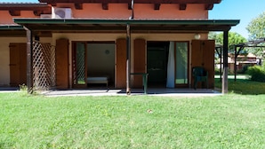 Un edificio de dos pisos con un porche cubierto, un pequeño jardín y una silla verde afuera.
