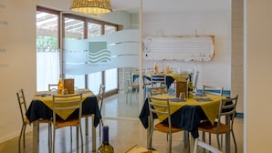 Un comedor con mesas dispuestas para dos, sillas y una botella de vino sobre la mesa.