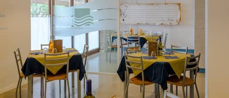 Un espace repas avec des tables dressées pour deux personnes, des chaises et une bouteille de vin posée sur la table.