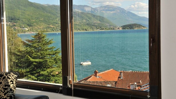 Una habitación con un ventanal que ofrece vistas a un lago, montañas y un bote.