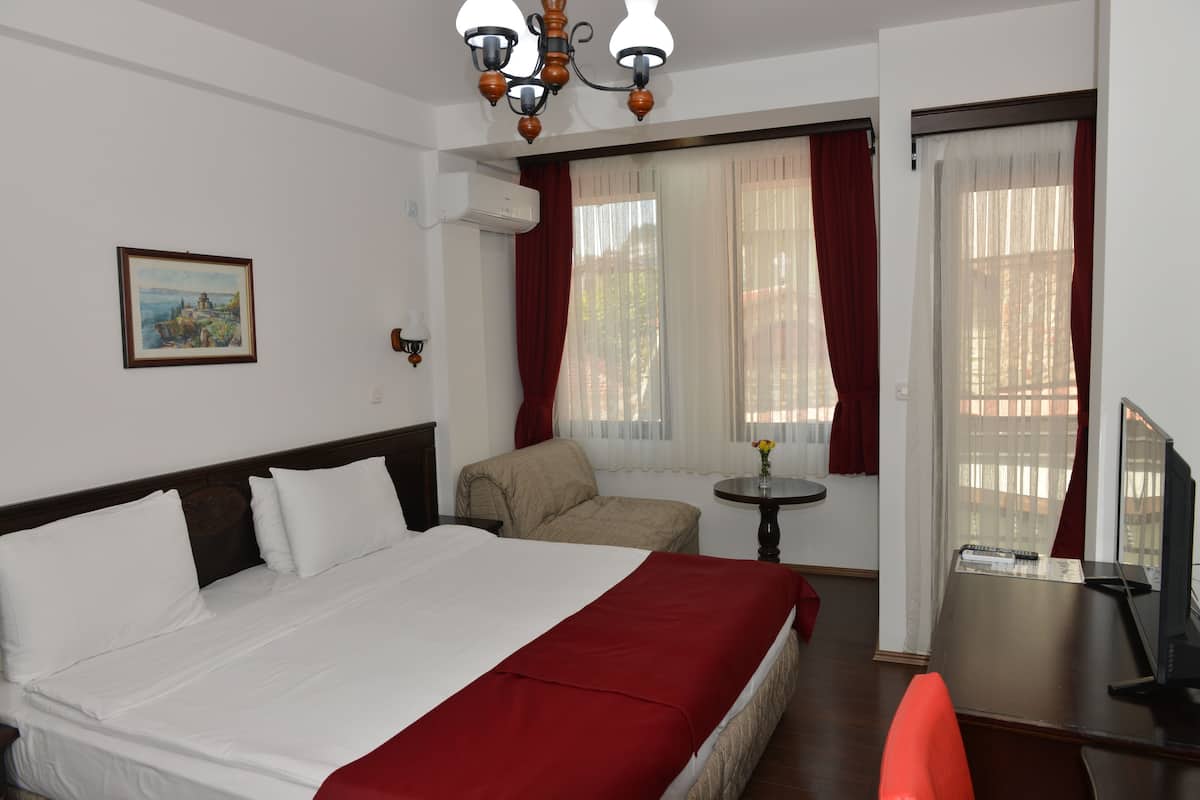 A hotel room with a large bed, a desk, a chair, and a small table with a vase.