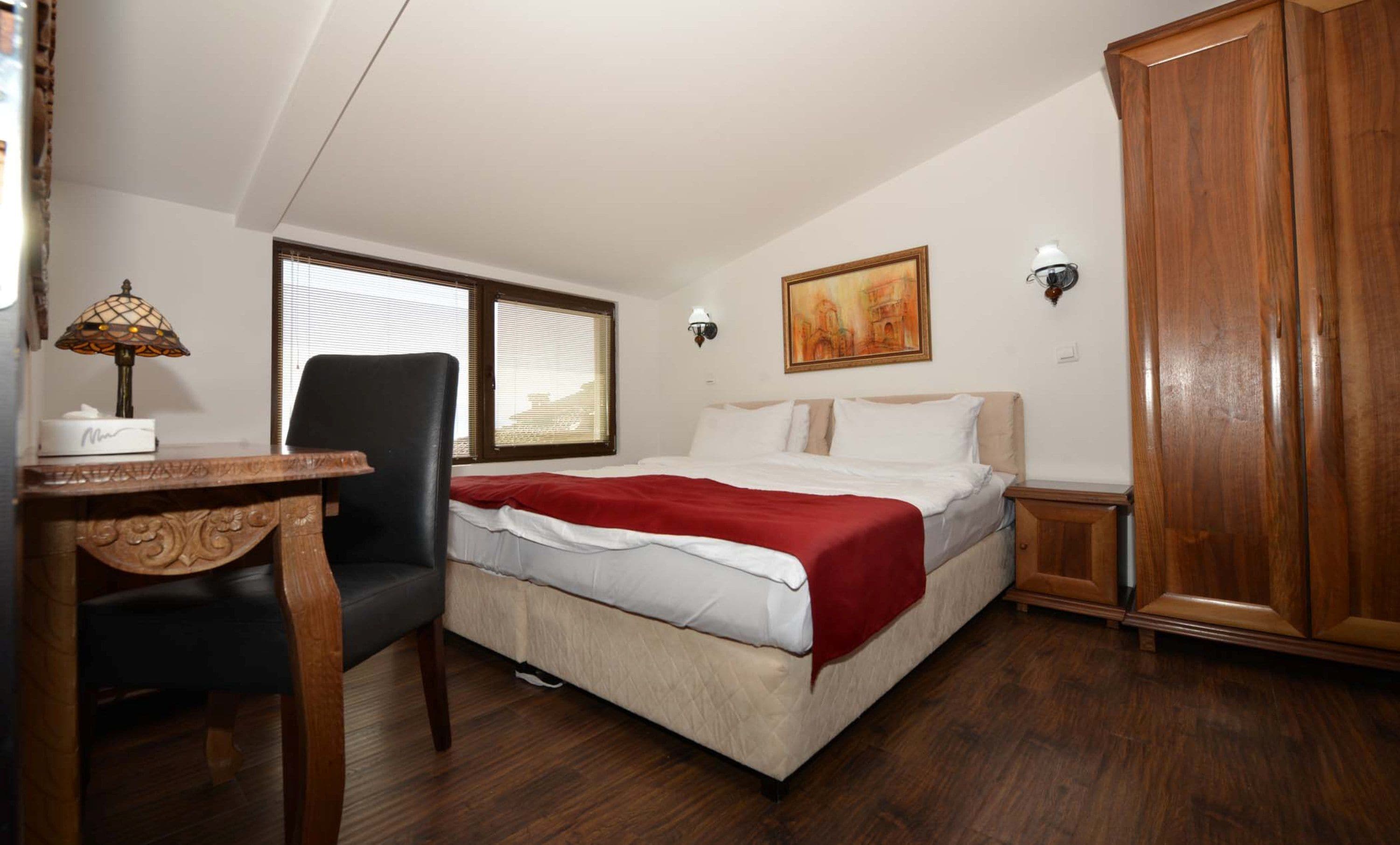 A bedroom with a bed, a desk, a chair, a wardrobe, and two windows.