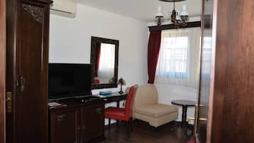 Una habitación con un armario de madera, televisor, silla, una mesita y una ventana con cortinas.