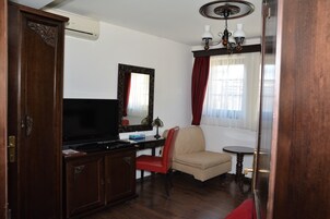 Una habitación con un armario de madera, televisor, silla, una mesita y una ventana con cortinas.
