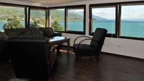 Habitación con vistas a un lago y montañas, que incluye un sofá, una mesa y una silla.