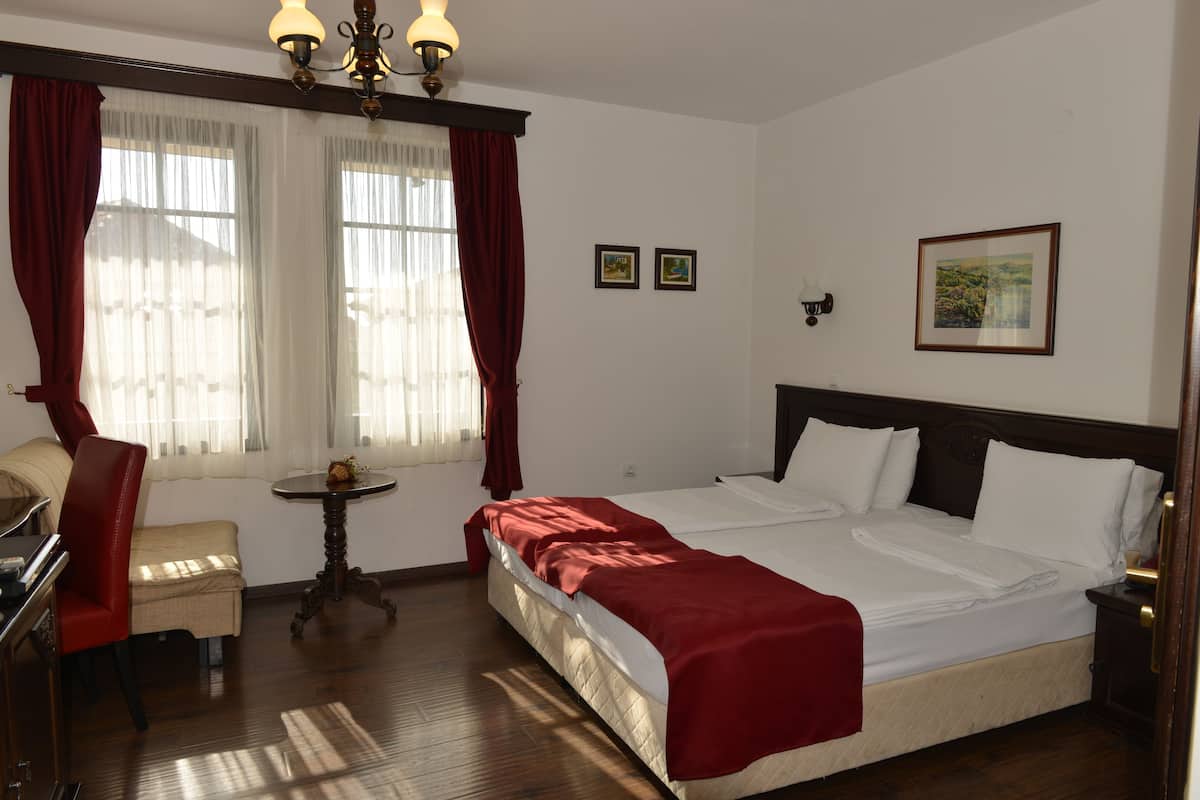 A hotel room with a bed, a desk, a chair, a small table, and a window with curtains.