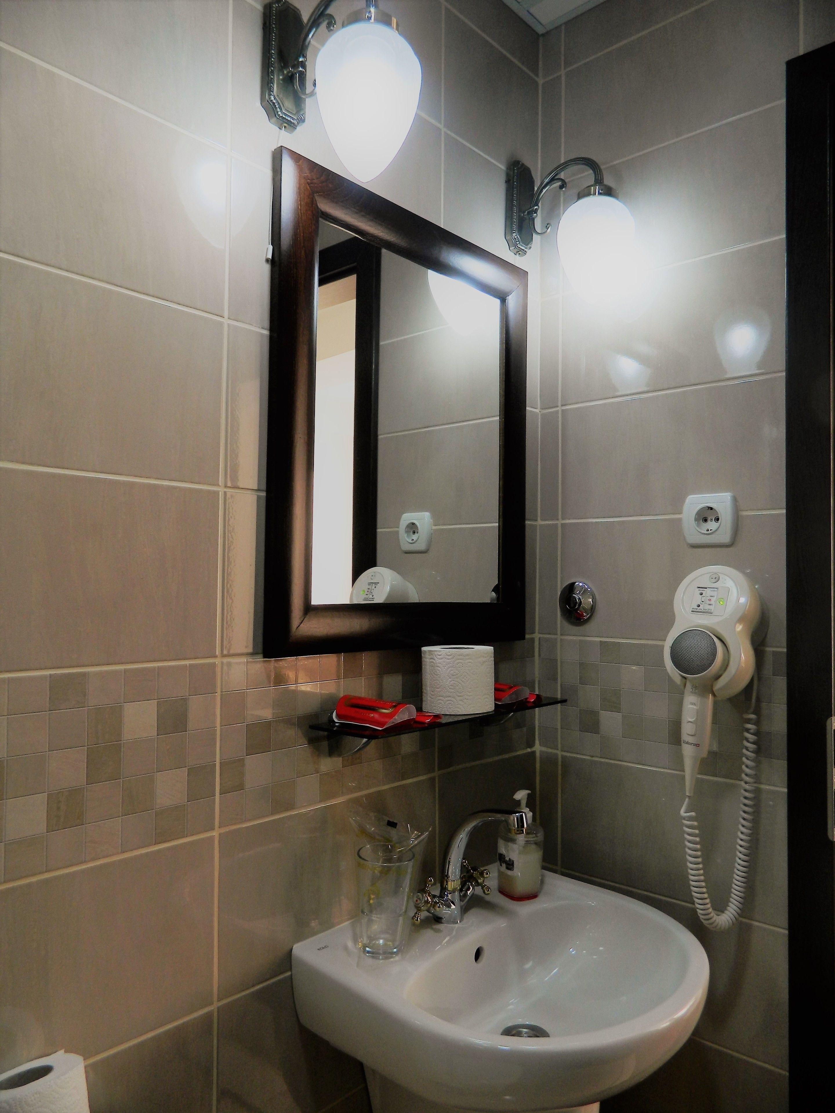 Un baño con lavabo, espejo y secador de pelo fijado a la pared.