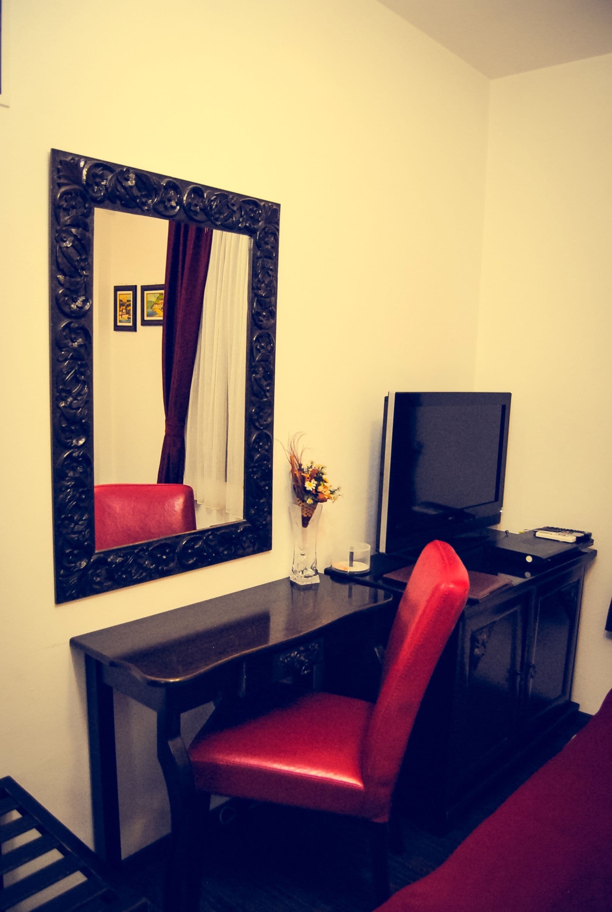 A room with a dark wooden desk, a red chair, a flat-screen TV, and a large ornate mirror.