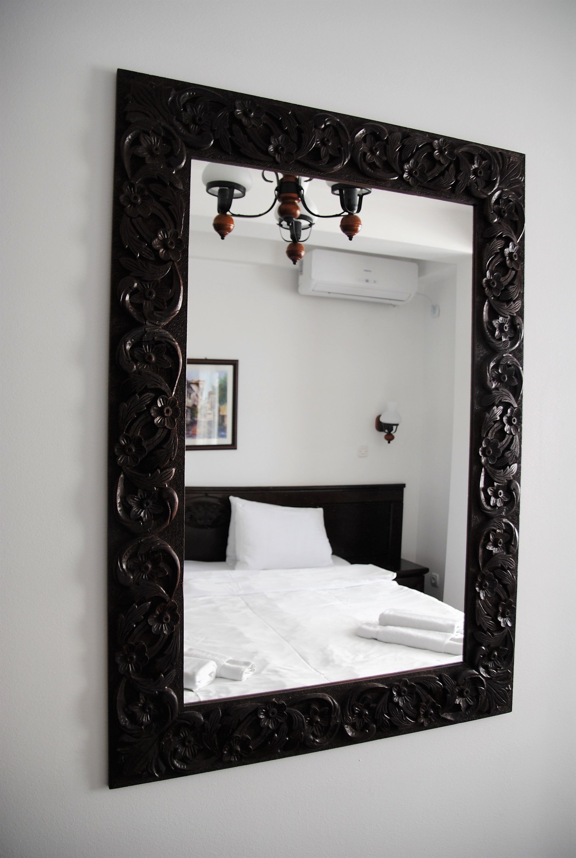 A bedroom with a large ornate mirror, a neatly made bed, and a wall-mounted air conditioning unit.
