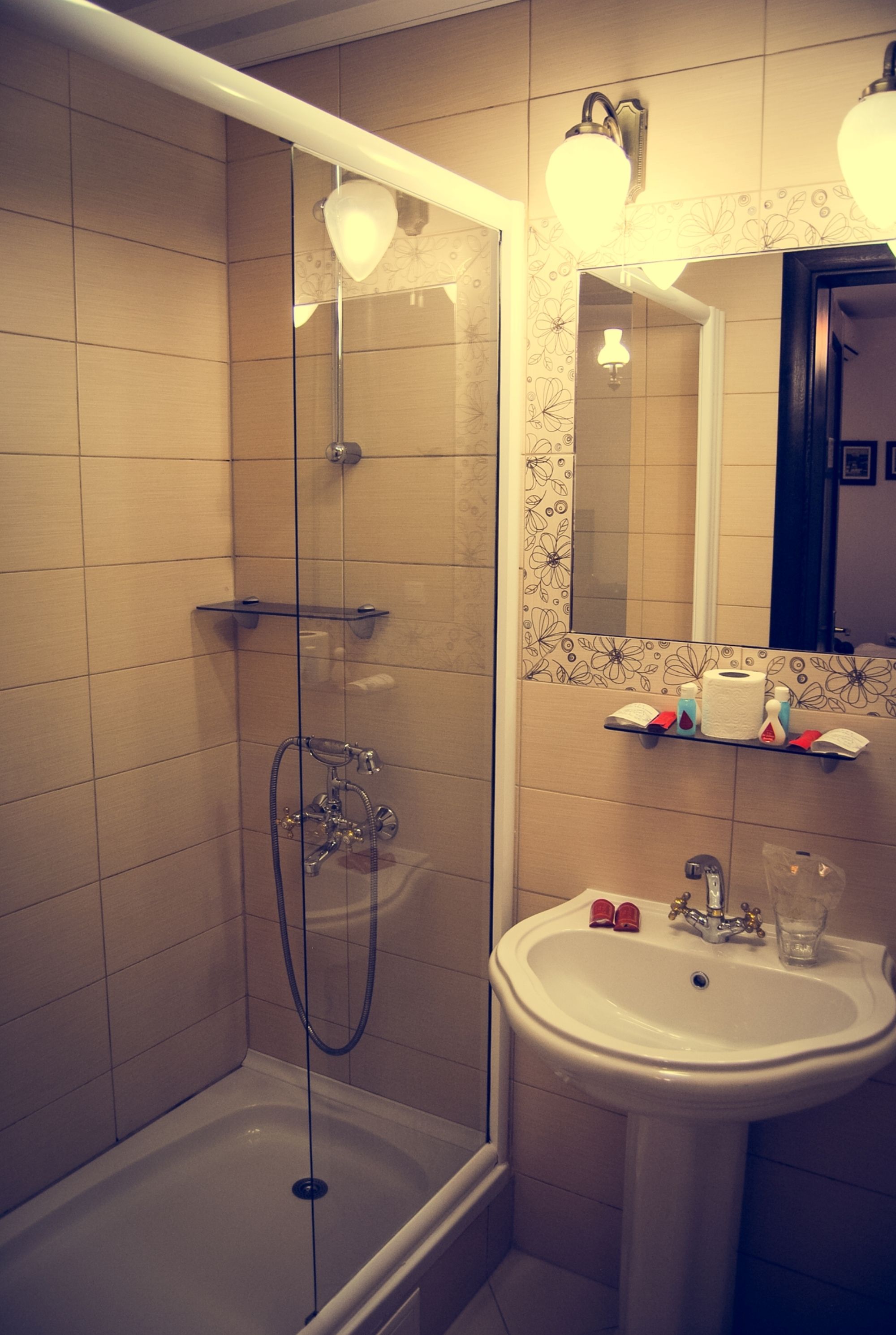 A bathroom with a glass-enclosed shower, a sink, and a mirror with a floral tile border.