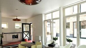A modern kitchen with white cabinets and a red backsplash, a dining area with white chairs and a wooden table, and large windows offering a view of the outside. - Themen Hotel zur Kranengasse (Kranenburg)