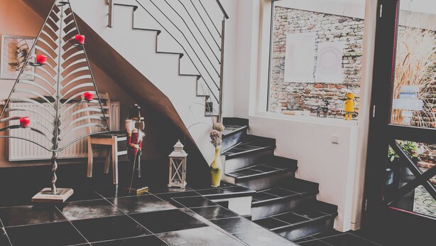 A staircase with a metal railing, a wooden chair, a small table, and a vase with flowers. - Themen Hotel zur Kranengasse (Kranenburg)