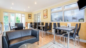 Un espace repas avec des tables et des chaises, un canapé et un téléviseur fixé au mur.
