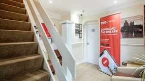 Un hall d’hôtel doté d’un escalier recouvert de moquette, d’un comptoir de réception et d’une banderole publicitaire pour l’application OYO.