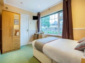 A bedroom with a bed, a wardrobe, a desk, a television, and a window with curtains.