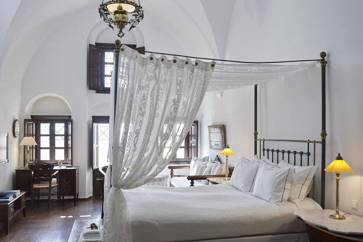 Una cama con dosel y mosquitera, un escritorio con silla, y una lámpara en una mesita de noche.