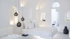 Un dormitorio minimalista y blanco con una cama, lámparas colgantes y una mesita de noche con un libro.