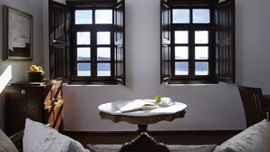 Una habitación con dos ventanas, una mesa con un libro y una taza, y vista al mar.