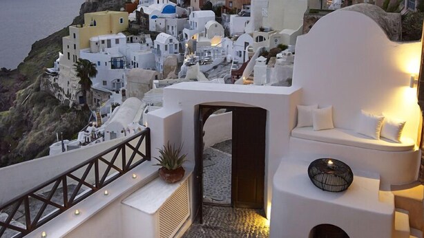 Terraza en la azotea con zona de estar, una mesa pequeña y vistas a un pueblo costero con edificios blancos.