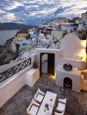 A rooftop terrace with outdoor seating, a view of a coastal town, and a sunset. - 1864 The Sea Captain's House (Santorini)