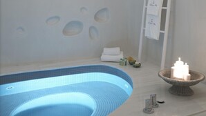 Un cuarto de spa con una bañera de hidromasaje con azulejos azules, un perchero blanco y una vela sobre un pedestal.