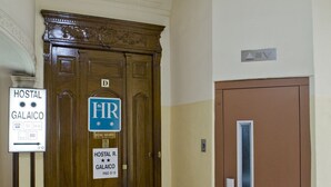 A hotel entrance with a wooden double door, a sign for 'Hostal R. Galaico Piso 5 D', and a smaller door to the right. - Hostal Galaico (Madrid)