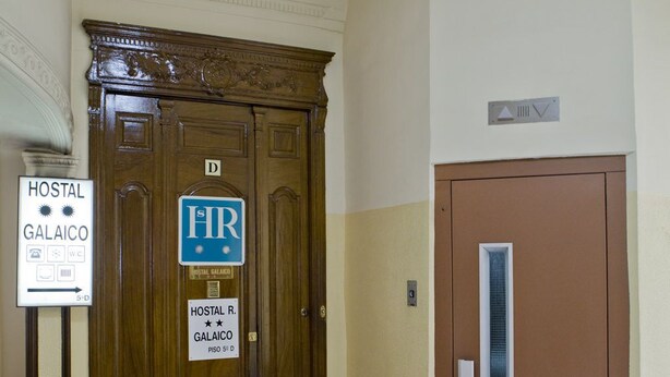 A hotel entrance with a wooden double door, a sign for 'Hostal R. Galaico Piso 5 D', and a smaller door to the right. - Hostal Galaico (Madrid)