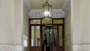 A grand hallway with marble flooring, a chandelier, and a wooden door leading to another room. - Hostal Galaico (Madrid)