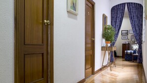 A hallway with wooden flooring, a wooden door, and a painting on the wall. - Hostal Galaico (Madrid)