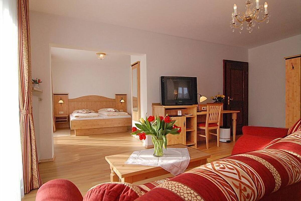 Une chambre d’hôtel avec un lit, un bureau avec une télévision, un canapé rouge et un vase rempli de fleurs rouges.