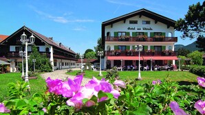 Een hotel met een rood-wit gevel, balkons met bloembakken, en een tuin met paarse bloemen op de voorgrond.