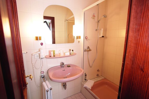 Un baño con un lavamanos rosa, una bañera y una ducha. Hay un espejo sobre el lavamanos y un marco de puerta de madera.