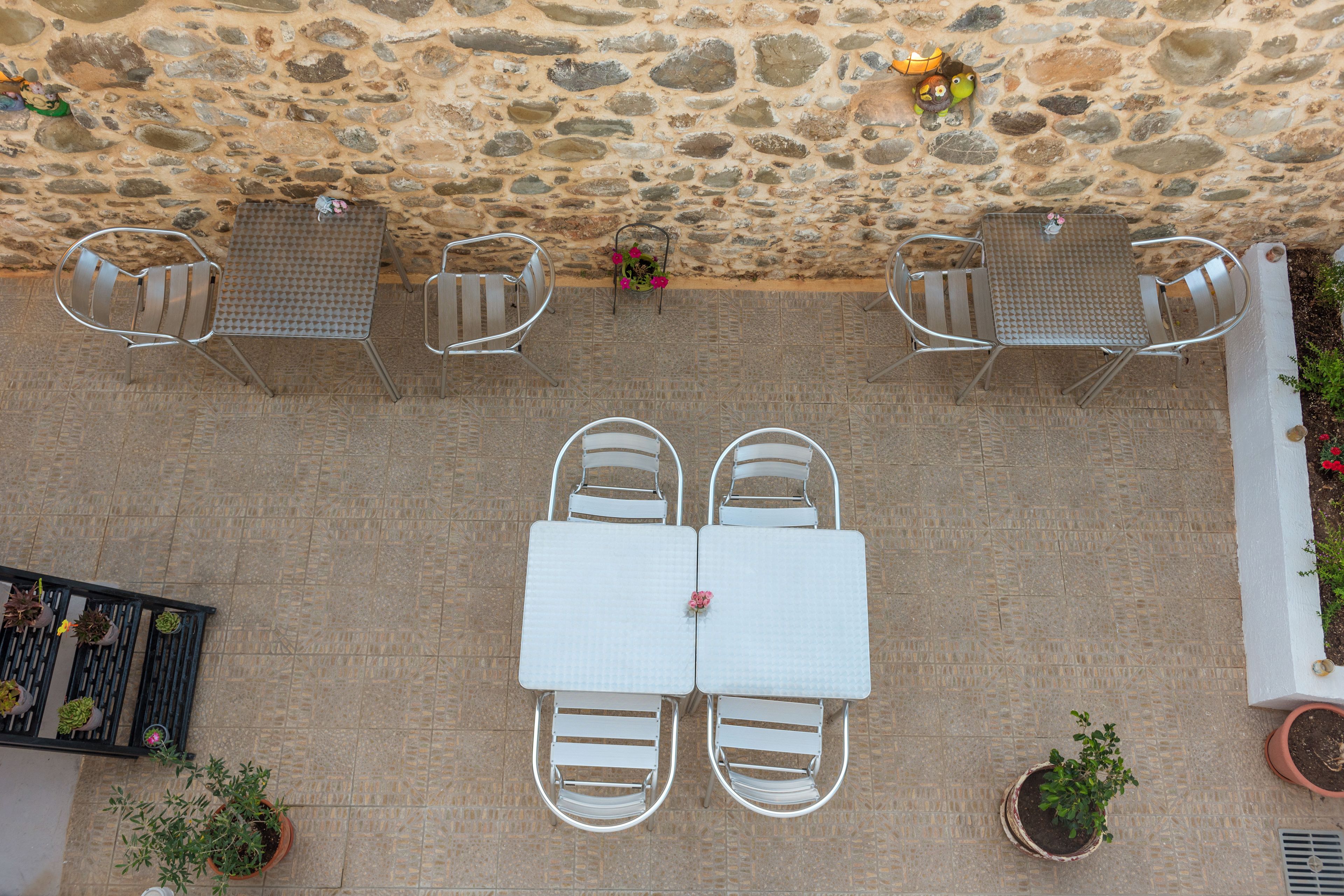 Un mur de pierre, deux tables avec des chaises et des plantes en pot.